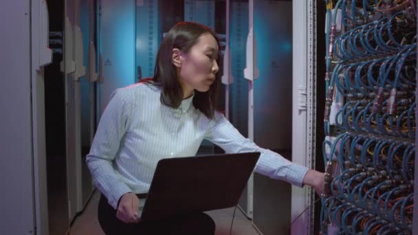 データセンターのスイッチや他のコンピューティング機器をチェックするためにラップトップを使用して女性アジアのネットワークエンジニアの追跡ショット — ストック動画
