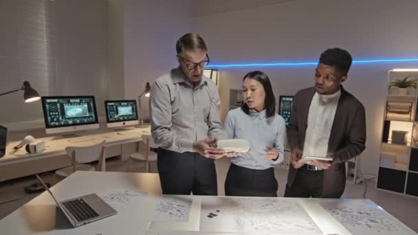 三位男女工程师慢吞吞地检查办公室里的打印汽车模型 讨论摆在桌面上的工作蓝图 — 图库视频影像
