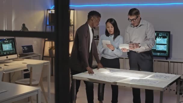 オフィスでテーブルの周りに立つエンジニアの多様なチームの追跡とDプリントカーモデルと設計図を議論 — ストック動画