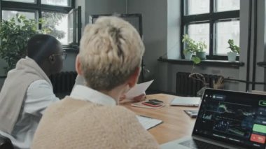 Değişik erkek ve kadın iş adamlarının sunduğu uyuşukluk diz üstü bilgisayarları ve finansal belgelerle büyük ahşap masada oturmuş yeni proje detaylarını tartışıyor.