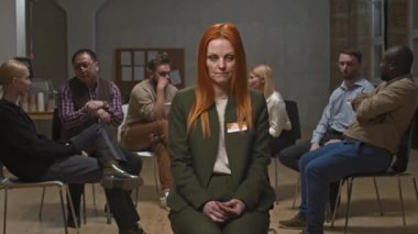 Diğer üyeler arka planda psikologla sohbet ederken, zihinsel destek grubu oturumunda bipolar bozukluğu olan, kameraya poz veren orta boy kadın portresi