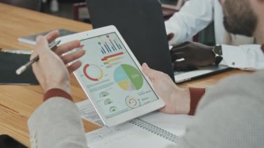 Dijital tablet ekranındaki yatırım veya finansal grafikleri ve diyagramları analiz ederken tanınamayan işadamlarının yavaş yavaş yaklaşımı masadaki meslektaşlarının önünde oturuyor.