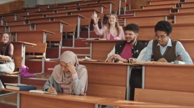 Lise ya da üniversite öğrencilerinin, utangaç Müslüman kızla dalga geçmeleri ve buruşuk kağıtları fırlatıp, büyük konferans salonundaki ahşap masalarda oturmaları.