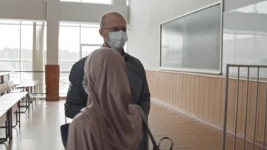Orta yaşlı erkek orta yaşlı üniversite profesörünün yüz maskesi takması öğrencilerin ders başında sıcaklıklarını ölçmek için temas kurulamayan kızılötesi termometre kullanıyor.