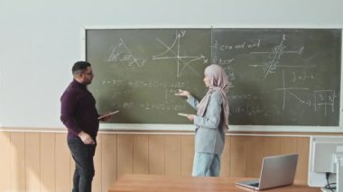 Erkek orta yaşlı matematik profesörü, Geometri problemini çözmek için Müslüman kadın öğrencilere karatahtanın önünde birlikte durmalarında yardımcı oluyor.