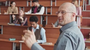 Cesur orta yaşlı profesörün karatahtaya işaret eden erkek ve kadın öğrencilerden oluşan küçük bir gruba ders verirken dikiz görüşlü yavaş çekim.