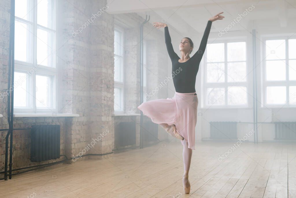 Young beautiful woman ballet dancer dressed in professional outfit pointe shoes and white tutu dancing in studio