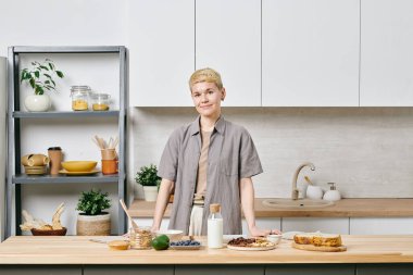 Mutfakta büyük ahşap bir masanın önünde duran ve sana bakan biri.