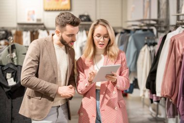 Bir erkek ve bir kadın giyim mağazasındaki tablet ekrandaki ürünlere bakıyor.