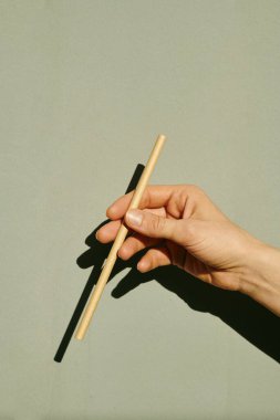 Gri duvarın üzerinde kameranın önünde bir kadın sopası tutuyor.