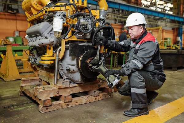 Manual worker in helmet examining the metal equipment in the machinery factory