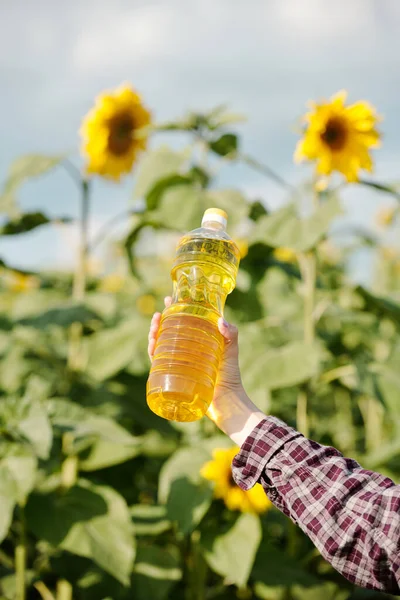 大きな黄色の花を持つ緑の植物に対して新鮮なひまわり油とプラスチックボトルを保持若い現代女性農家の手 — ストック写真