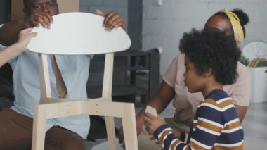 Dört kişilik Afro-Amerikan ailesinin yavaşça el kamerasıyla çekilmiş ve ahşap sandalyeyi bir araya getirişi.