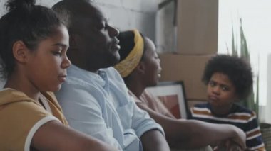Yeni evlerinde yerde oturup sohbet eden Afro-Amerikan anne ve babaların yan görüntüsü. Eşyaları karton kutularda.