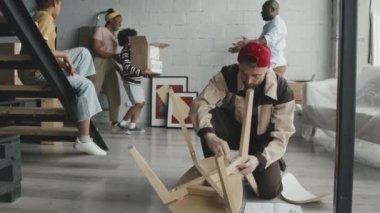 Üniformalı erkek işçinin yeni evine taşınan Afro-Amerikan aile için mobilya montajı yaparken yavaş çekimleri.