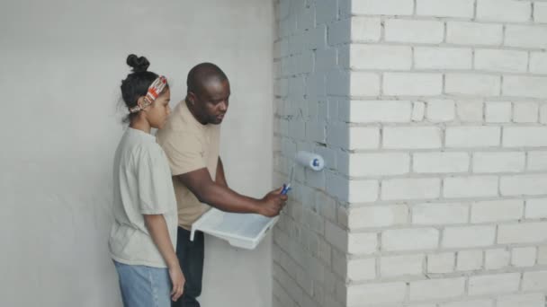 アフリカ系アメリカ人の父が娘にレンガの壁を描く方法を教えている間に撮影 — ストック動画