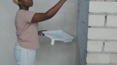 Kafasında bantla evi yenilerken tuğla duvar boyayan Afro-Amerikan kadını yavaş yavaş yukarı kaldır.