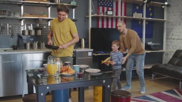 当他的男伴和顽皮的学龄男孩坐下来吃饭时 慢吞吞地拍着一个开开开心心的男人在吃早餐 — 图库视频影像