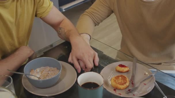 キッチンテーブルに座って朝食を取りながら手を取り合っている認識できない男性の手の高い角度の減速 — ストック動画