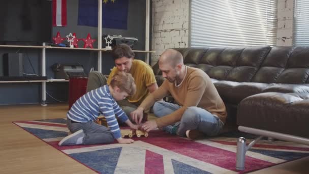 中等比例的快乐父亲和他们的小儿子坐在舒适的公寓里的地毯上 一起玩玩具 — 图库视频影像