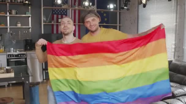 在舒适的公寓里 快乐的同性恋夫妇举着彩虹旗 微笑着拍照的慢镜头 — 图库视频影像