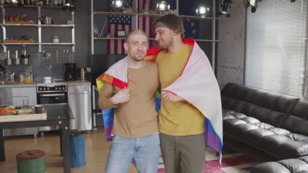 ゆっくりとポルノのショットの愛ゲイカップルとともに虹旗持って彼らの居心地の良いアパートとポーズのためにカメラ — ストック動画