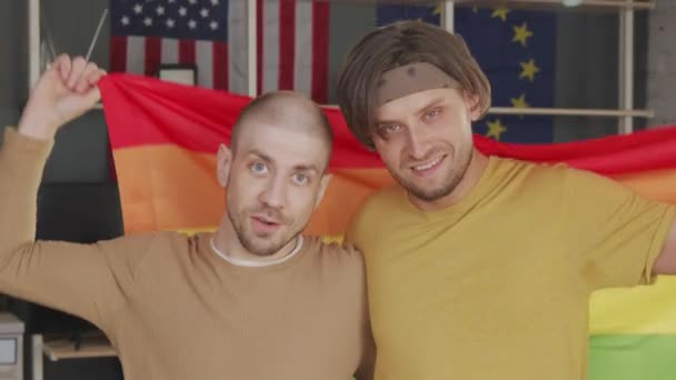 照片上的一对快乐的同性恋夫妇 带着彩虹旗 在他们的公寓里对着相机微笑 然后深情地望着对方 — 图库视频影像
