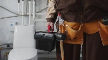 Boruları tamir ettikten sonra alet kemeri ve alet çantasıyla banyoda duran tanınmayan erkek tesisatçının orta kesiminde.