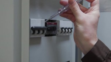 Tanımlanamayan erkek elektrikçinin tornavida kullanıp sigorta kutusundaki şalterleri incelerken yakın çekim.