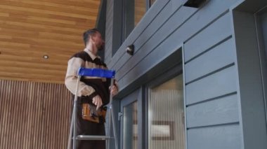 Üniformalı erkek müteahhitin merdivene çıkıp müşterilerin evinin dışına güvenlik kamerası yerleştirdiği el kamerasının yavaş çekimleri.