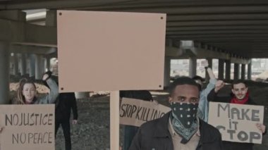 Otoyol köprüsünün altında dikilip kamera önünde protesto eden bir grup insanın yavaş çekimleri.