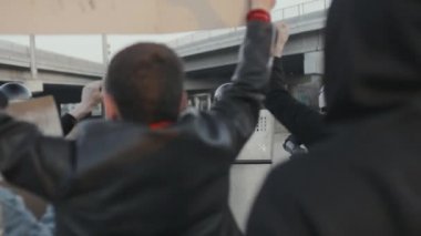 Bir grup genç protestocunun slogan atan ve caddeleri kapatan kalkanlı çevik kuvvet polisleriyle yüzleşen el kameraları görüntüleri.
