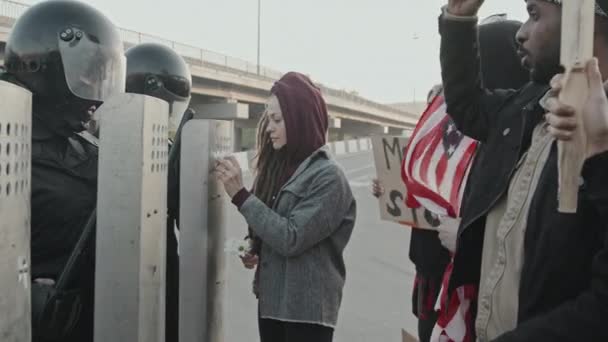 看板や米国の旗が抗議している間 恐ろしいロックを持つ若い女性のスローモーション追跡ショットは 暴動警察のシールドに花を入れて — ストック動画