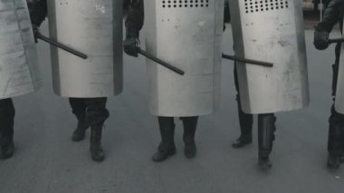 Tanımlanamayan çevik kuvvet polislerinin yavaş çekimleri protesto sırasında kalkanlarını coplarla dövüyor ve yürüyorlar.