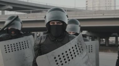 Kalkan ve cop tutan çevik kuvvet polisinin yavaş çekimleri ve kamera önünde poz vermek için yürürken diğer polisler de arkasında sıraya girdiler.