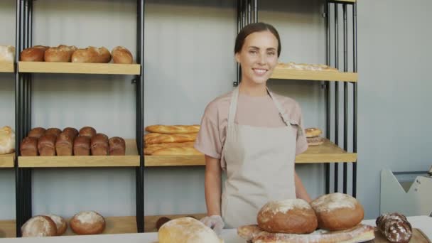 幸せな若い女性カウンターアテンダントのスローモで撮影された肖像画を追跡します 棚の上にパンの焼きたての愛と居心地の良いパンでポーズ — ストック動画