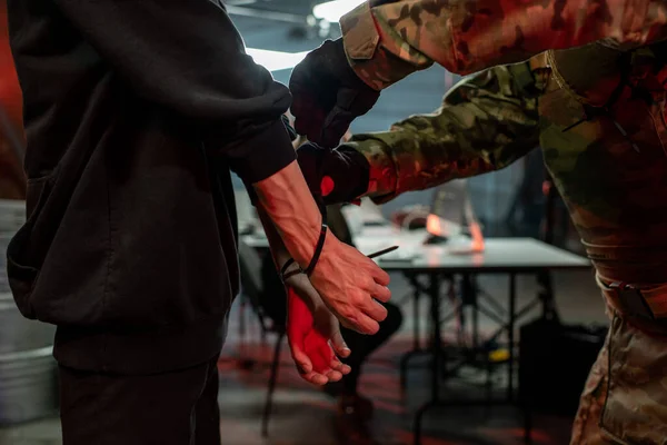 Officer in military outfit putting cuffs on captured criminal — Stock Photo, Image