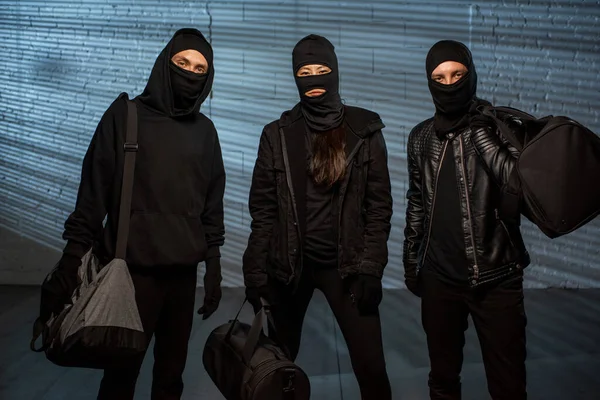 Três ladrões em roupa preta carregando bolsas — Fotografia de Stock