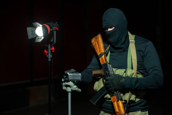 Soldado em balaclava e luvas preparando câmera para gravação de confissão criminal — Fotografia de Stock