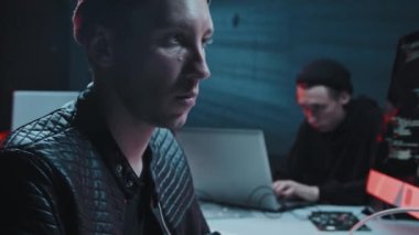 El bilgisayarı yavaş çekimde, şapka ve ceket giyen erkek hacker 'lar kredi kartı veya banka kartına bakıp bilgisayardan veri veya para çalarken karanlık bir yerde saklanıyorlar.