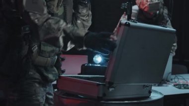Özel kuvvetler memurlarının hacker 'ların saklandığı yere baskın yaparken yavaş çekimde biri bilgisayarı kontrol ederken diğeri de evrak çantasını kontrol ediyor.