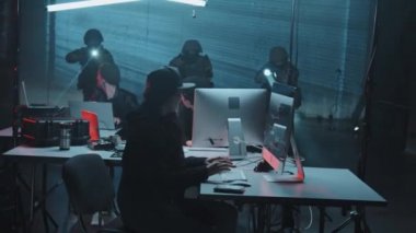 Silahlı SWAT ekibinin yavaş çekimleri elinde fenerlerle suçlu hackerların karanlık saklandığı yeri basıyor ve bir kadın kaçarken iki adamı tutukluyor.