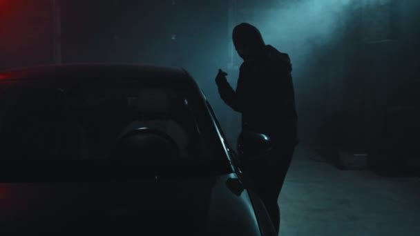 暗いガレージに駐車車に侵入マスク強盗の遅い追跡ショット — ストック動画