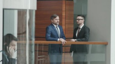 Meslektaşları cam asansörle telefonda konuşurken, takım elbiseli, kendinden emin iki erkek avukatın ofiste sohbet ederken orta yavaş çekimleri.