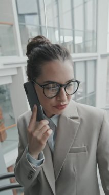 Ofisteki cam asansörle aşağı inerken gözlüklü ve resmi kıyafetli genç bayan avukatın dikey yavaş çekimi.