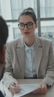 Formalite ve gözlük takmış genç bayan avukatın omuzlarının üstünden geçen dikey yavaşlığı iş sözleşmesinden soyutları okurken müvekkiline hukuki konularda danışıyor.