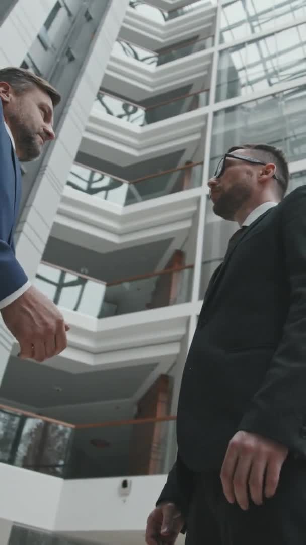近代的なオフィスで屋内に立つ民事裁判所の成功の結果の後に手を振る成熟したビジネスマンや彼の弁護士の垂直低角度ショット — ストック動画