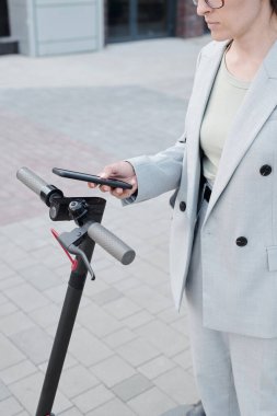 Takım elbiseli modern bir kadın bir süreliğine scooter kiralayacak.