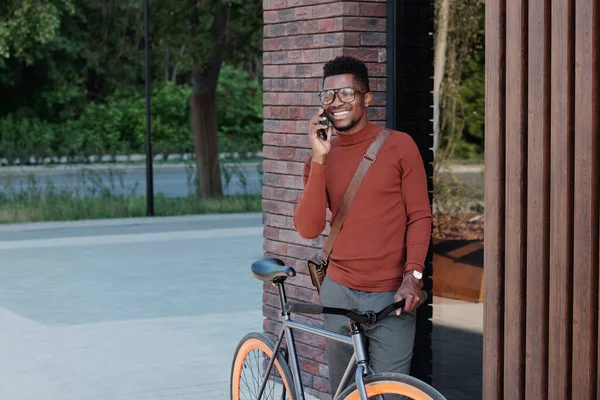 Modern binadan bisikletli genç Afrikalı iş adamı arıyor. — Stok fotoğraf