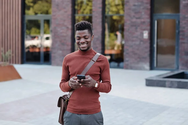 Gelukkige jonge zakenman van Afrikaanse etniciteit met behulp van smartphone — Stockfoto